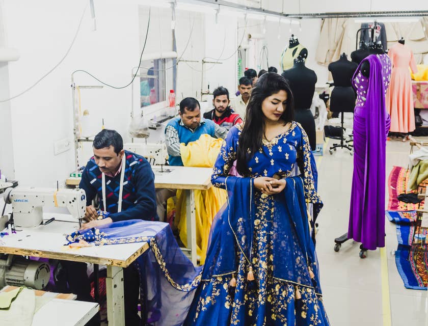 Woman wearing blue bespoke dress while tailor does finishing touches.