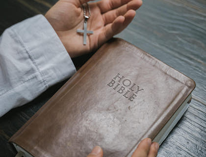 A man's hands holding a Bible and a cross.