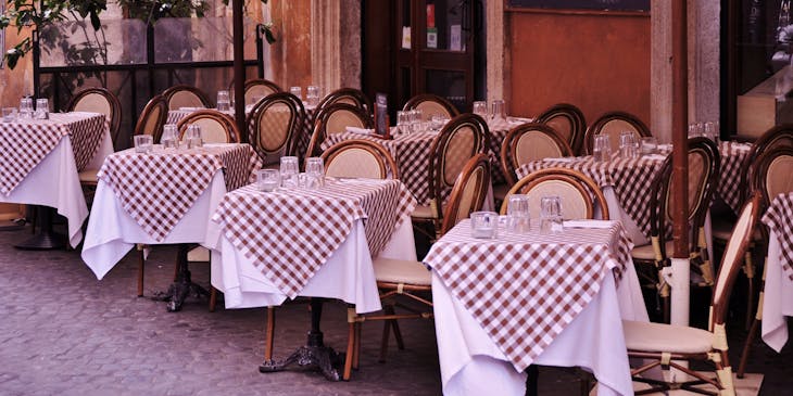 A bistro with small square tables with checkered table cloths outside on a cobblestone sidewalk.