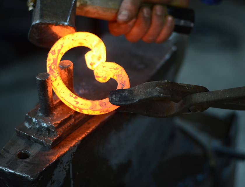 Un herrero dando forma a una pieza de metal en un negocio de herrería.