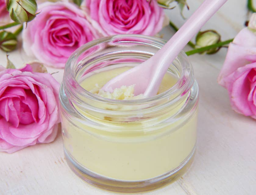 Petit pot de beurre corporel avec cuillère rose entouré de roses roses dans une entreprise de beurre corporel.