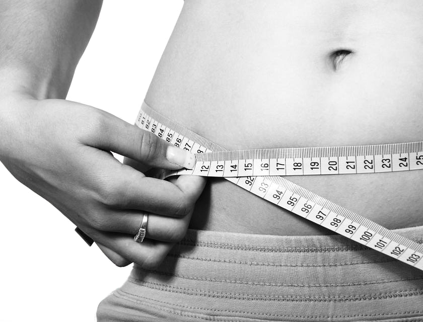 Eine Frau misst vor einem Body Sculpting mit einem Maßband ihren Bauchumfang.