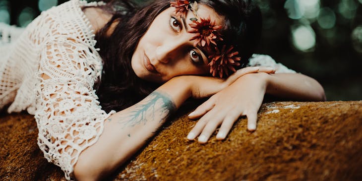 Boho woman with tattooed wrist in crocheted top and flower crown lying on a rock