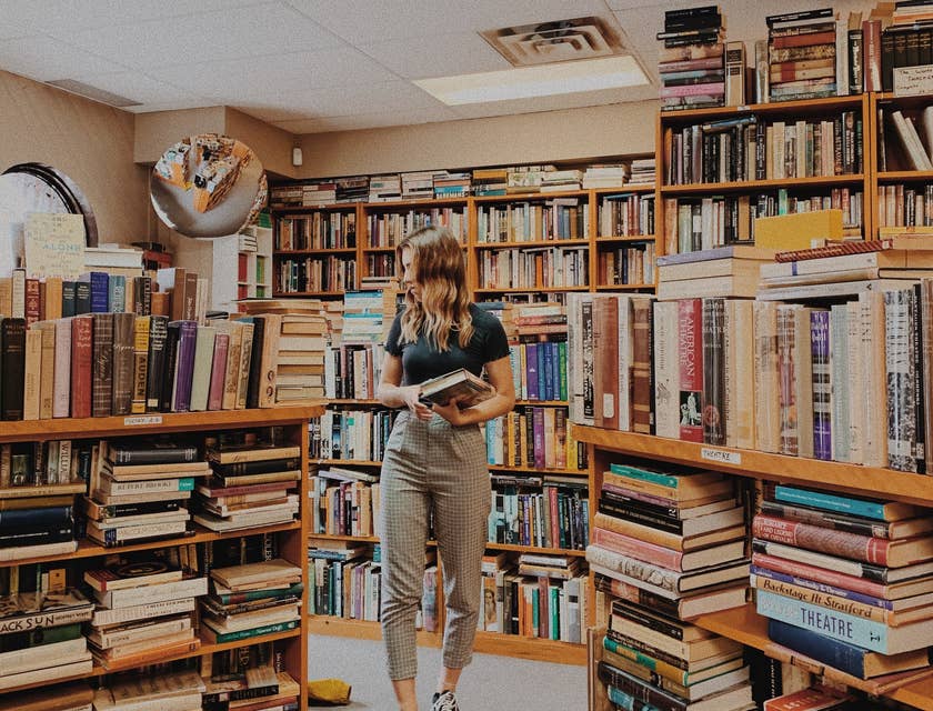 Una mujer sosteniendo un libro en medio de un negocio de libros.