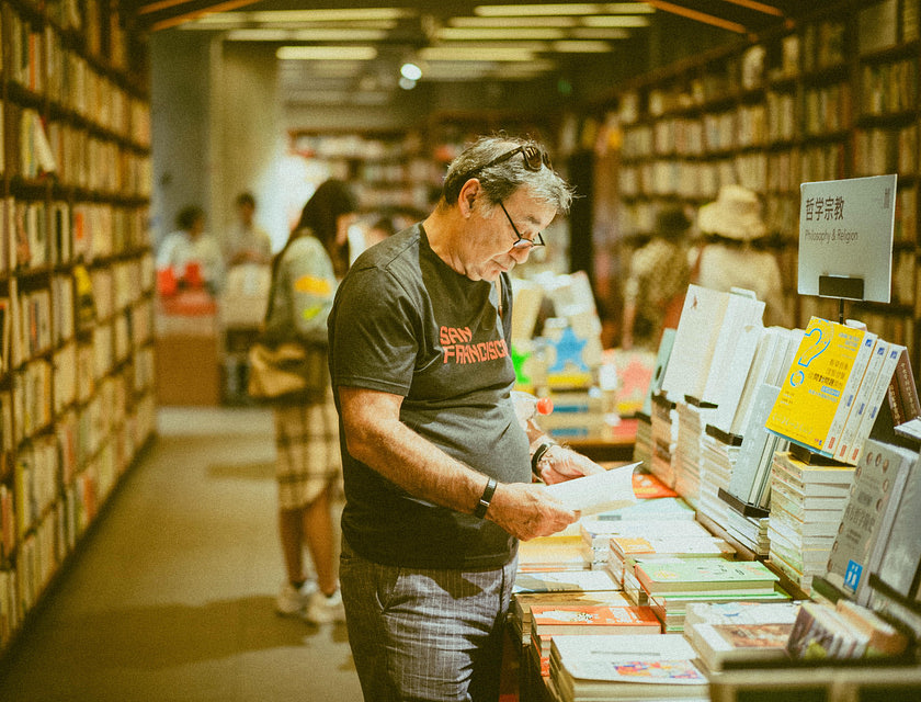 Un uomo che legge un libro dentro una libreria.