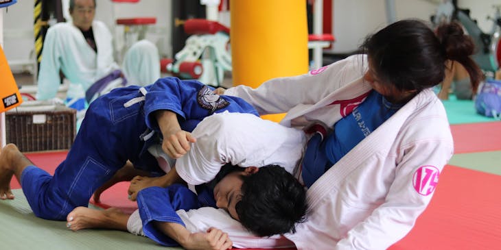Man and woman in white and blue uniforms practicing Brazilian Jiu-Jitsu.