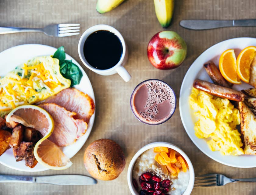 Zwei herzhafte Frühstücksteller mit Eiern, Speck, Würstchen, Obst, Joghurt und Kaffee stehen auf einem Tisch in einem Café.