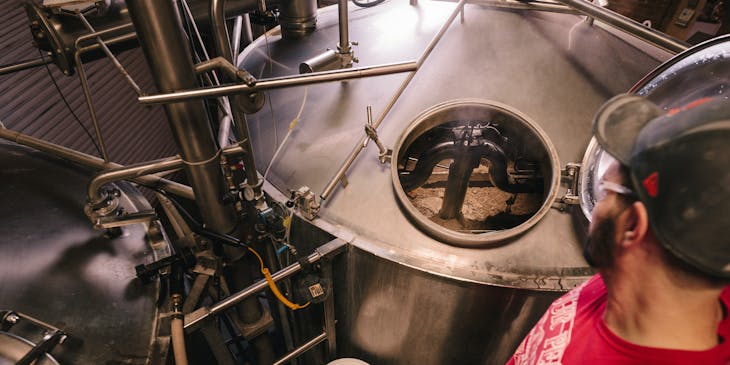 A man inspects a large beer fermenter at a brewery.