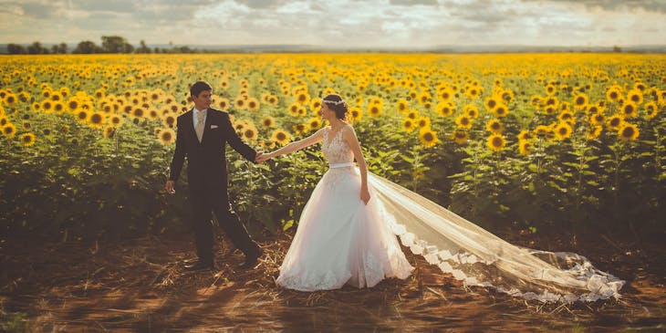 Bride and groom walking in a sunflower field.
