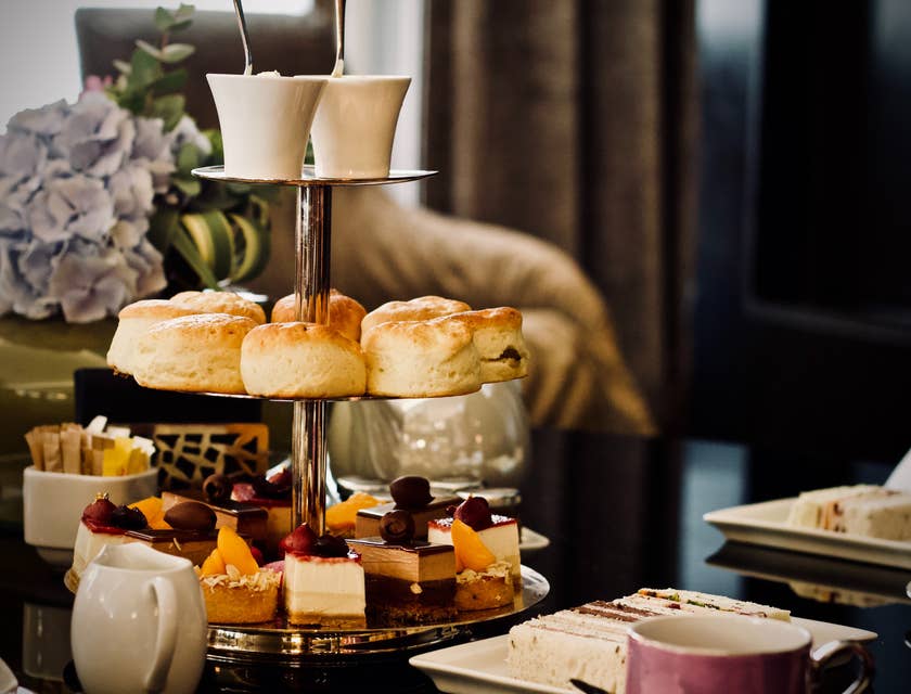 Mesa com xícaras de chá, minibolos e scones em restaurante britânico.