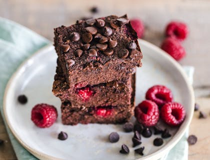 Tres brownies apilados uno encima del otro con frutos rojos por un lado en un plato de cerámica blanca.