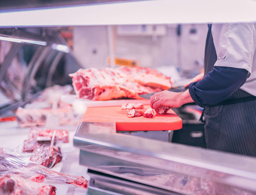 Açougueiro cortando carne crua em tamanhos pequenos em um açougue.