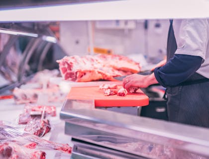 Un boucher découpant de la viande crue en petits morceaux dans une boucherie.