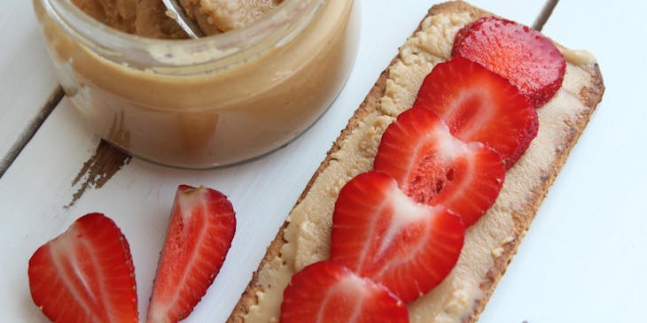 A jar of homemade butter and strawberries displayed on a white table.
