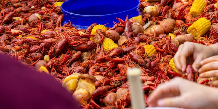 People sharing a Cajun seafood platter crawfish, corn, and potatoes.