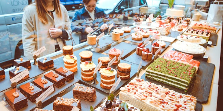 A woman stares through the window at treats in a cake shop.
