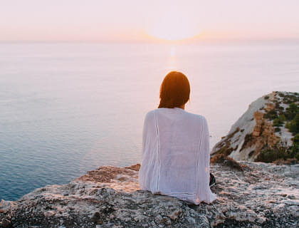 Una donna seduta su uno scoglio che guarda il mare calmo.
