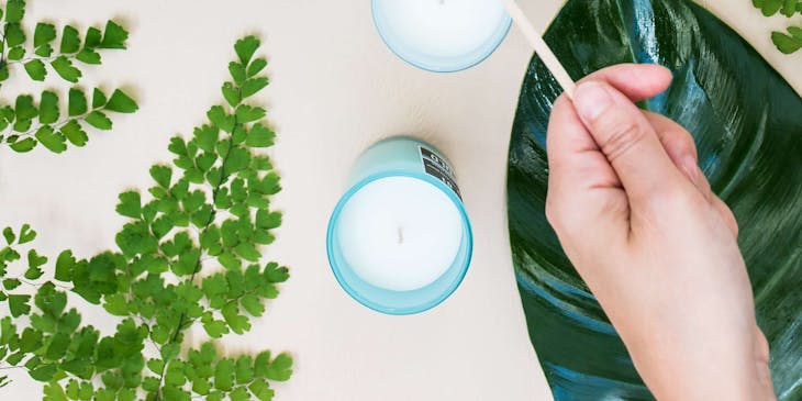 A hand lighting candles on a table with leaves.