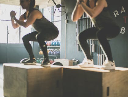 Pair of women preforming squat jumps in cardio class.