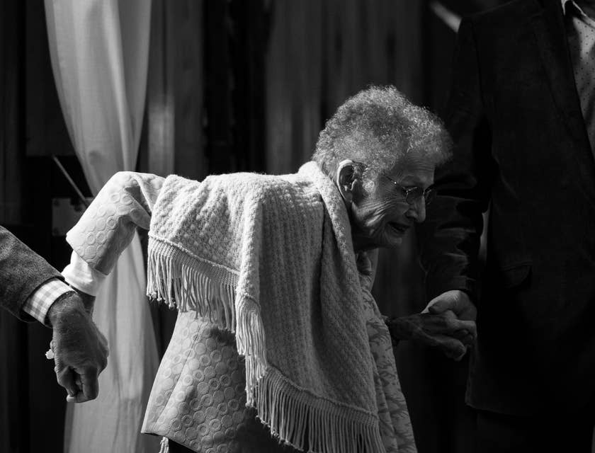 Deux auxiliaires de vie élégamment vêtus aidant une femme âgée à se mettre sur ses pieds.