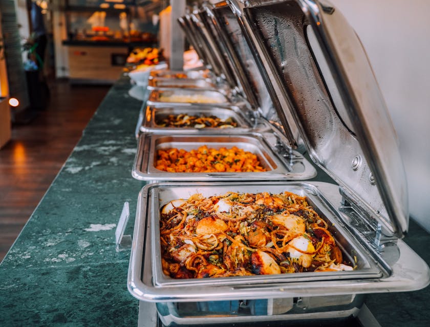 Uma variedade de comidas aquecidas em bandejas durante um serviço de catering.