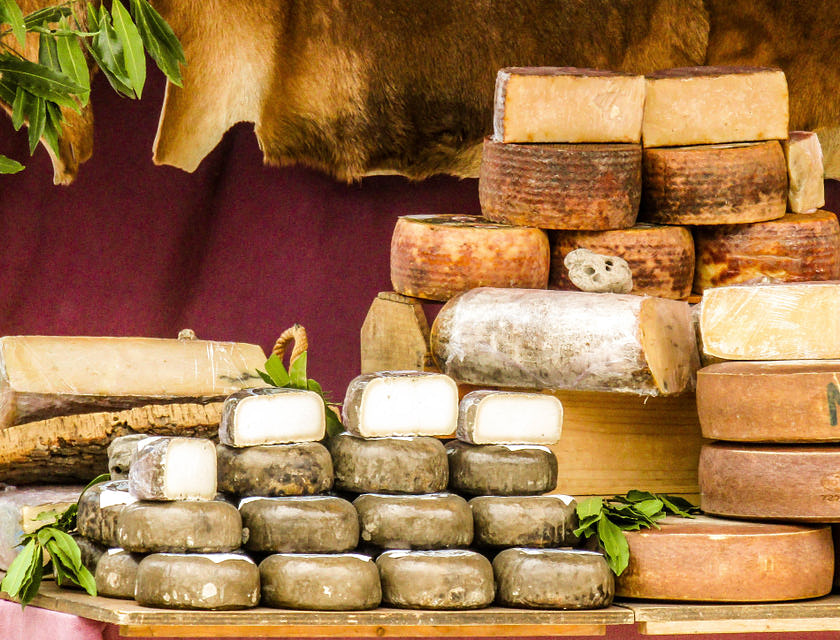 Varias columnas de ruedas de queso italiano sobre una mesa de madera frente a una cortina rojo carmesí en un negocio de tiendas de quesos.