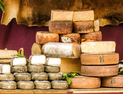 Varias columnas de ruedas de queso italiano sobre una mesa de madera frente a una cortina rojo carmesí en un negocio de tiendas de quesos.