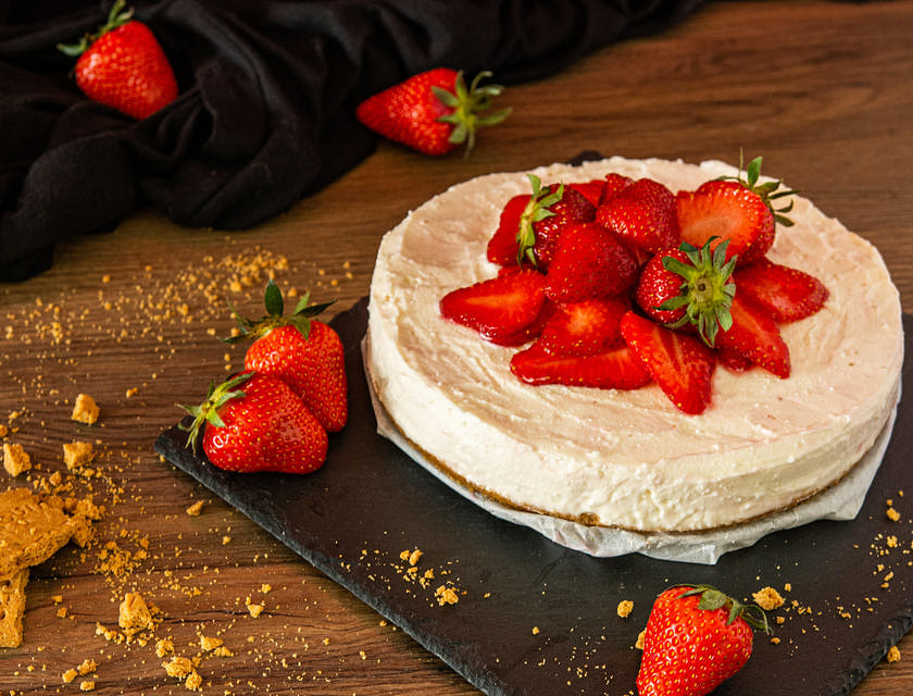 Un cheesecake garni de fraises sur une table en bois.