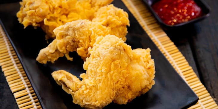 Tre ali di pollo fritte su un piatto nero.