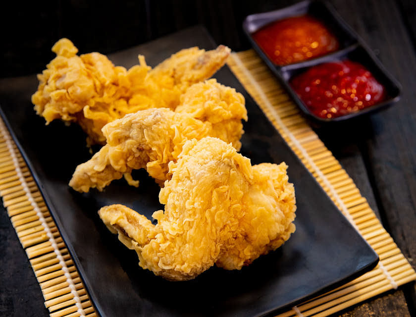 Drei frittierte Chicken Wings liegen neben zwei Soßen auf einem schwarzen Teller.