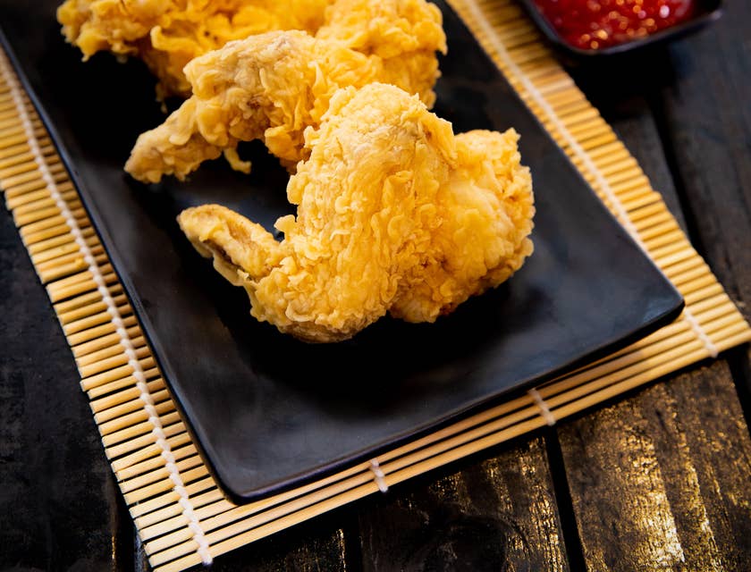 Drei frittierte Chicken Wings liegen neben zwei Soßen auf einem schwarzen Teller.