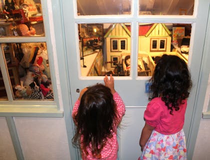 Two girls looking at a doll house display at a children's museum.