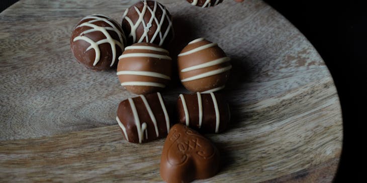 Hand picking up a milk chocolate truffle from a wooden board with more milk and dark chocolate truffles on top.