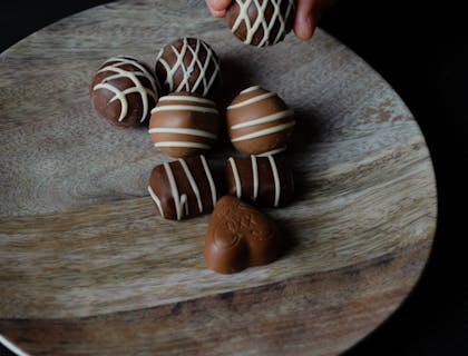 Hand picking up a milk chocolate truffle from a wooden board with more milk and dark chocolate truffles on top.