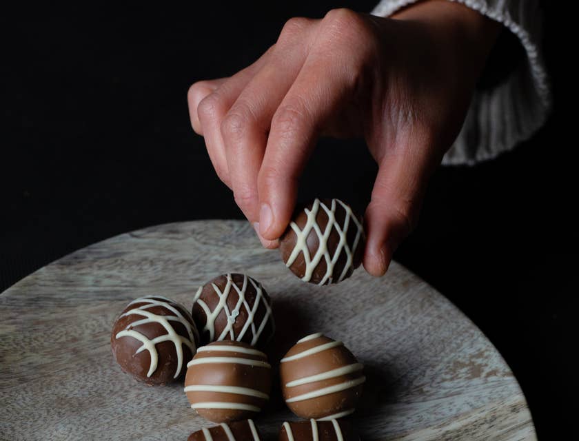 Hand picking up a milk chocolate truffle from a wooden board with more milk and dark chocolate truffles on top.