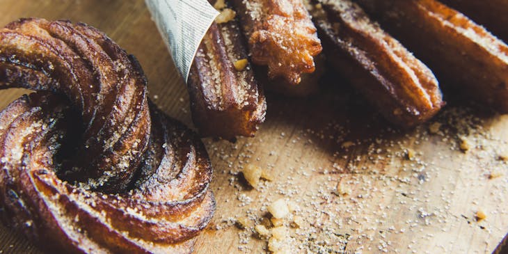 Sugar-dusted churros on a wooden cutting board.