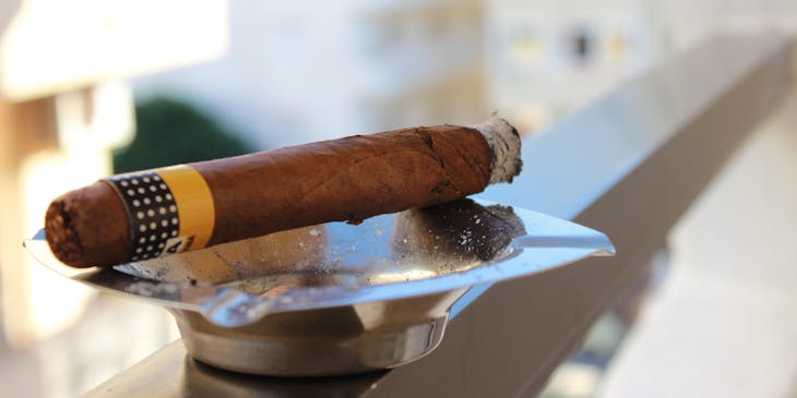 A cigar made by a cigar business balancing on a grey ashtray.