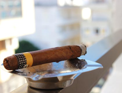 A cigar made by a cigar business balancing on a grey ashtray.