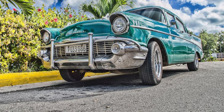A classic blue car pictured against a bright blue sky and palm trees.