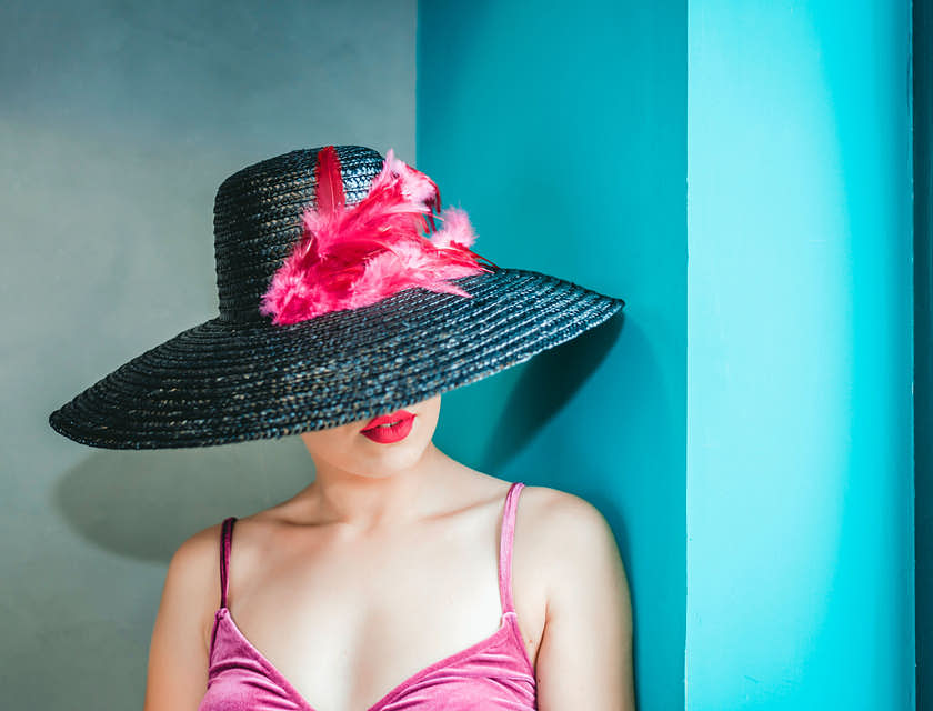 Une femme portant un chapeau à large bord orné de plumes roses.