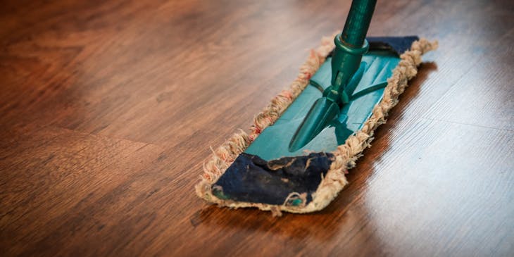 A person cleaning a wooden floor with a mop.