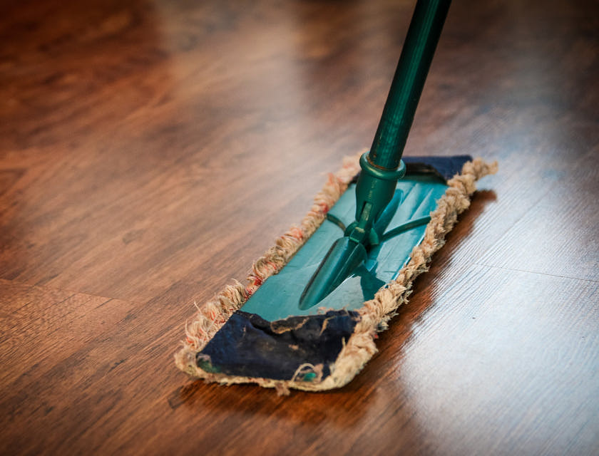 Persona limpiando el piso de madera con un trapeador en un negocio de limpieza.