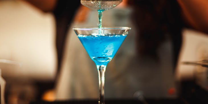 A person pouring a cocktail through a strainer at a cocktail bar.