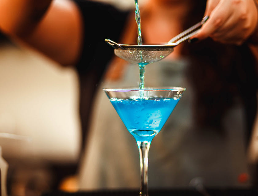 Pessoa preparando um drink azul em um bar de drinks.
