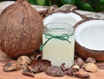 Un coco entero a un lado de un coco partido detrás de un frasco con aceite de coco sobre una mesa de madera en un negocio de coco.