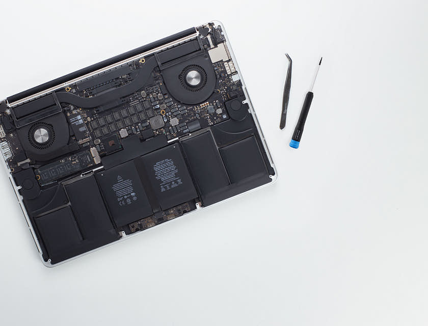 Ein Computerreparaturdienst arbeitet an einem Laptop ohne Plastikverkleidung mit einem Schraubenzieher und einer Pinzette.