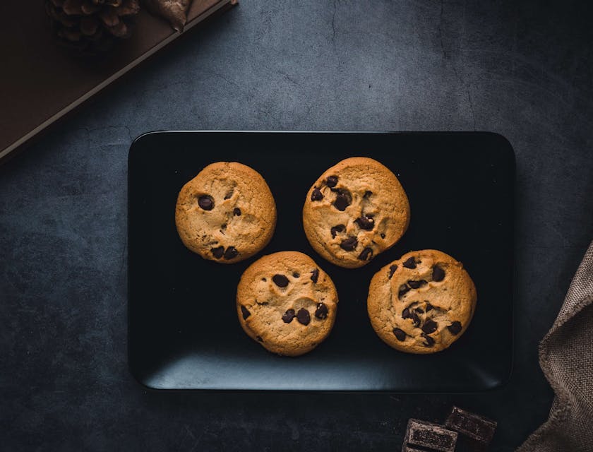 Four chocolate chip cookies in a black rectangular plate.