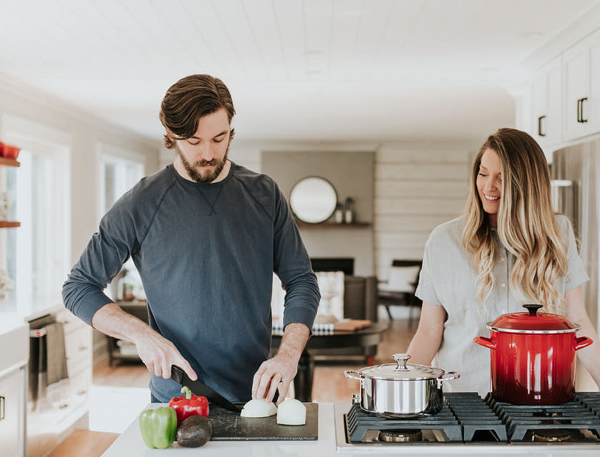 Une femme en train de regarder un homme qui coupe des légumes dans un cours de cuisine.