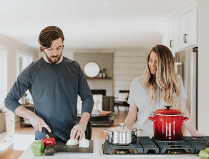 Mulher observando um homem cortar vegetais em um curso de culinária.