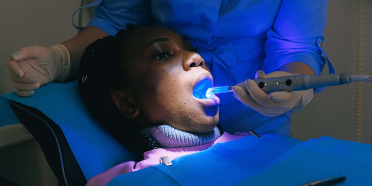Un·e dentiste cosmétique utilise une lampe à polymériser sur une patiente.